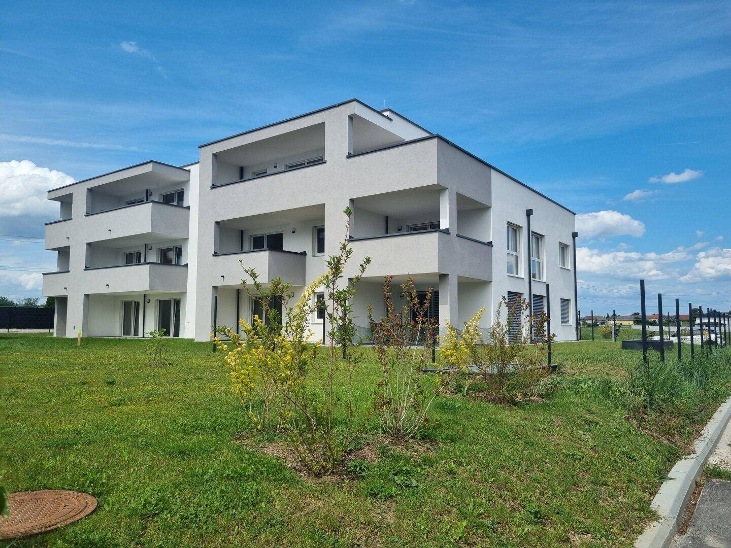 Modernes Mehrfamilienhaus mit Balkonen und Grünflächen unter blauem Himmel.