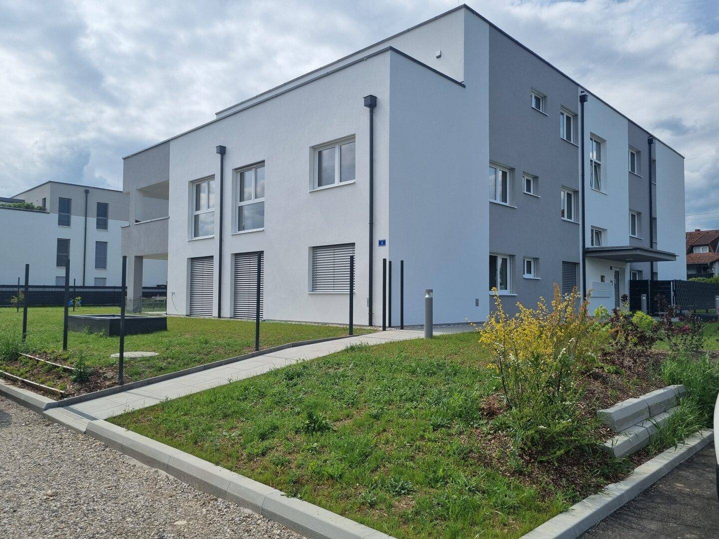 Neubau-Wohngebäude mit moderner Fassade, Fenstern und gepflegtem Vorgarten.