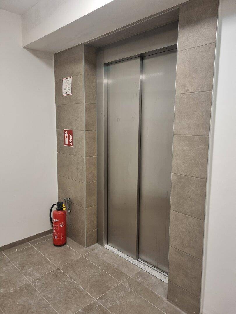 Moderner Aufzugsbereich mit Fliesenboden und Feuerlöscher im Gebäude.