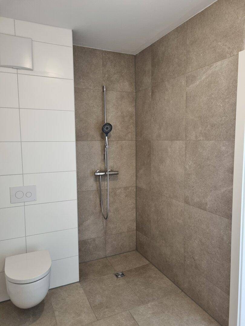 Modernes Badezimmer mit begehbarer Dusche, Wand-WC und grauen Fliesen.