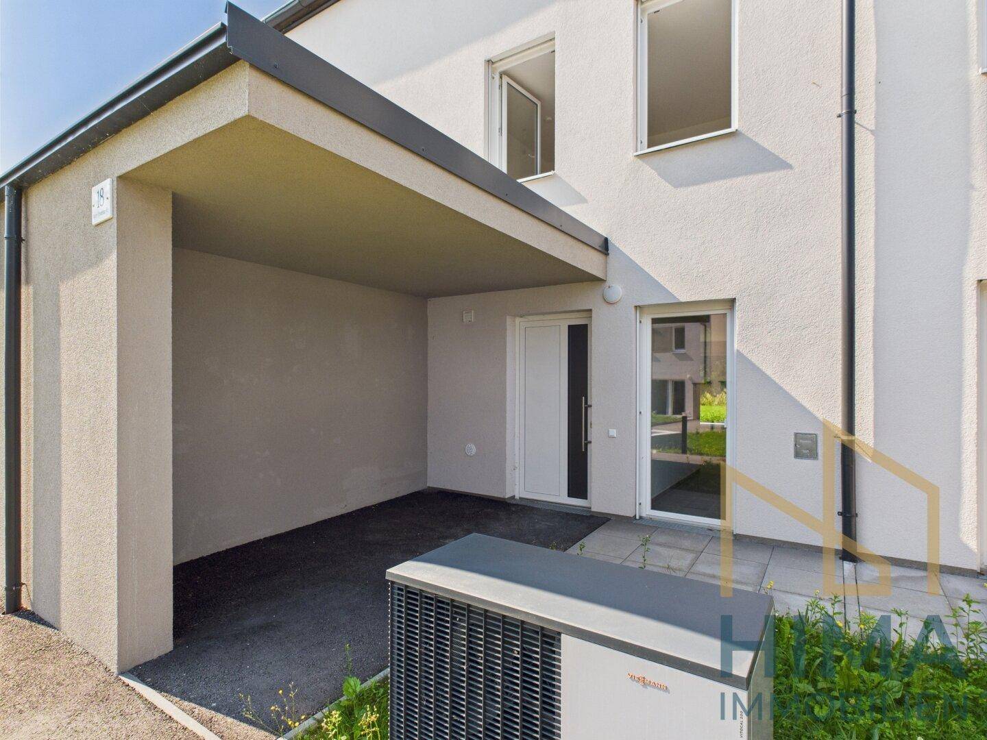Moderne Gebäudefassade mit Carport und effizienter Wärmepumpe im Außenbereich.