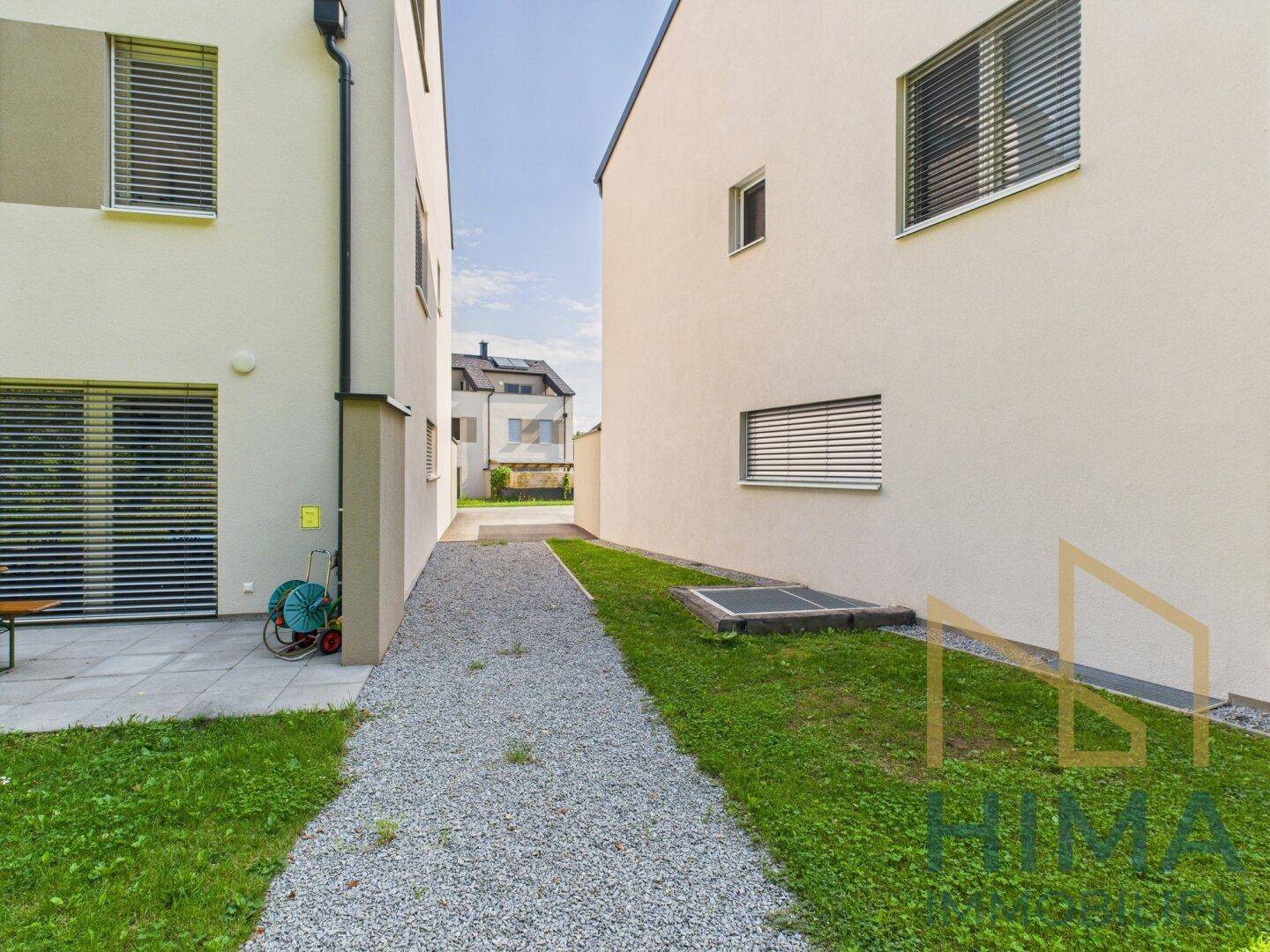 Zwischenraum zwischen zwei modernen Gebäuden mit Kiesweg und gepflegtem Rasen.
