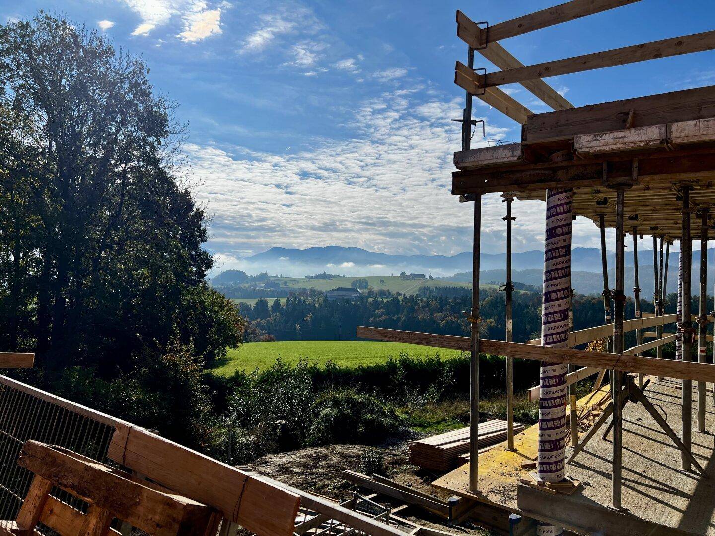 Panoramablick von der Baustelle über grüne Felder und die Berglandschaft.