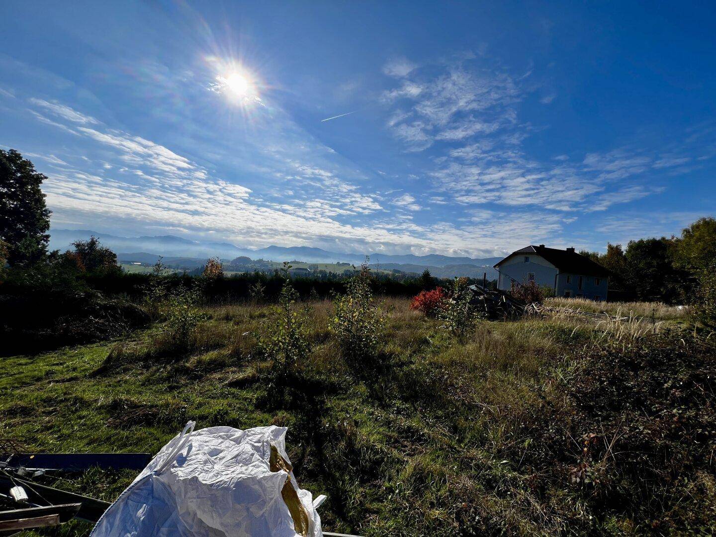 Sonniger Blick über das Grundstück mit ländlicher Umgebung und Bergsilhouette am Horizont.