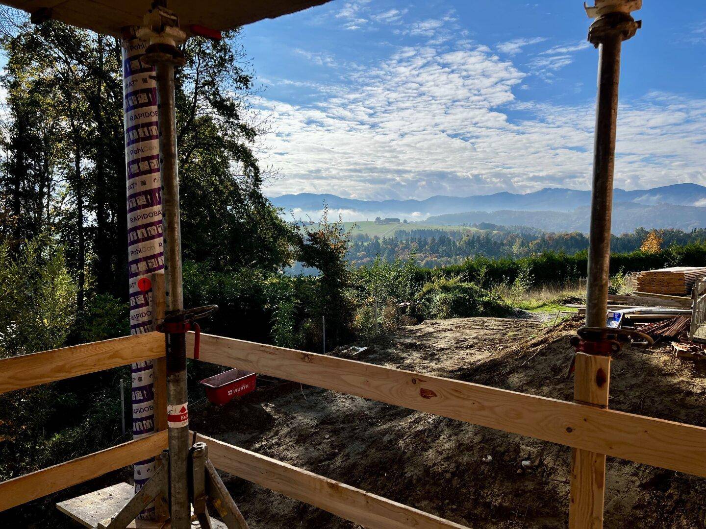 Blick von der Baustelle auf die weite Landschaft mit Bergen und bewaldeten Hügeln.