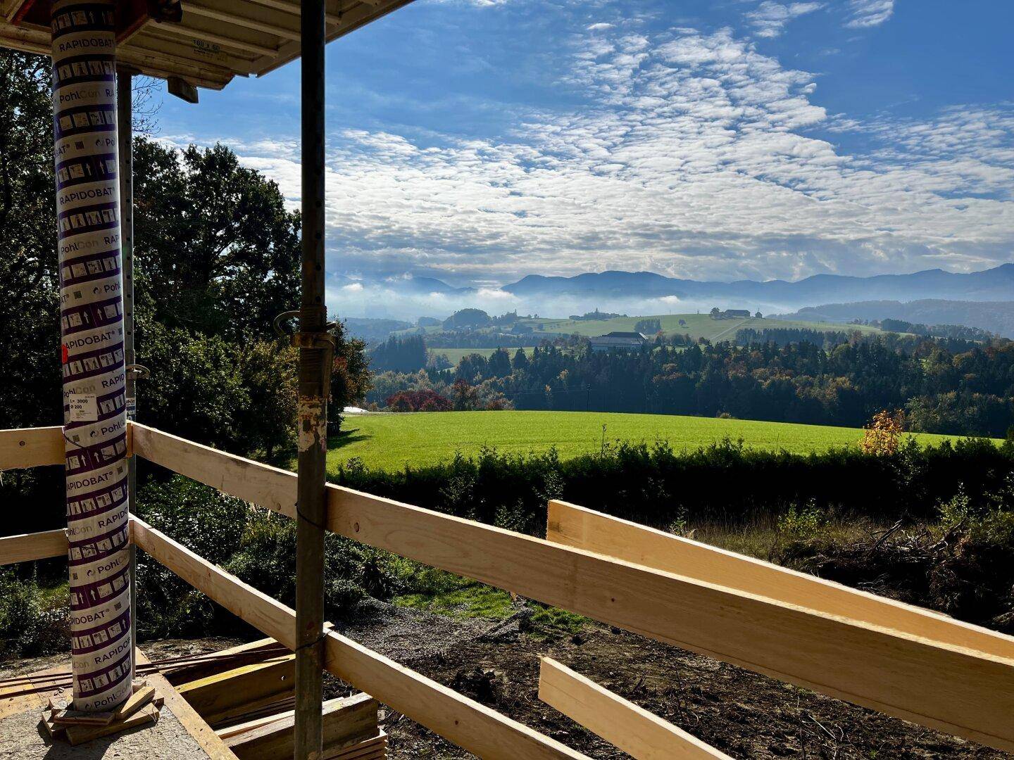 Weitläufiger Ausblick von der Baustelle auf die hügelige Landschaft und die Bergkette am Horizont.