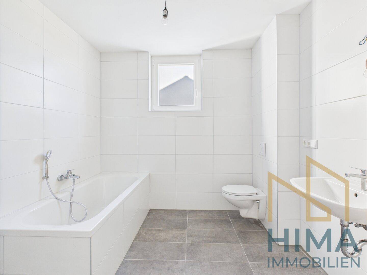 Modernes Badezimmer mit weißen Wandfliesen, Badewanne, WC und Fenster.