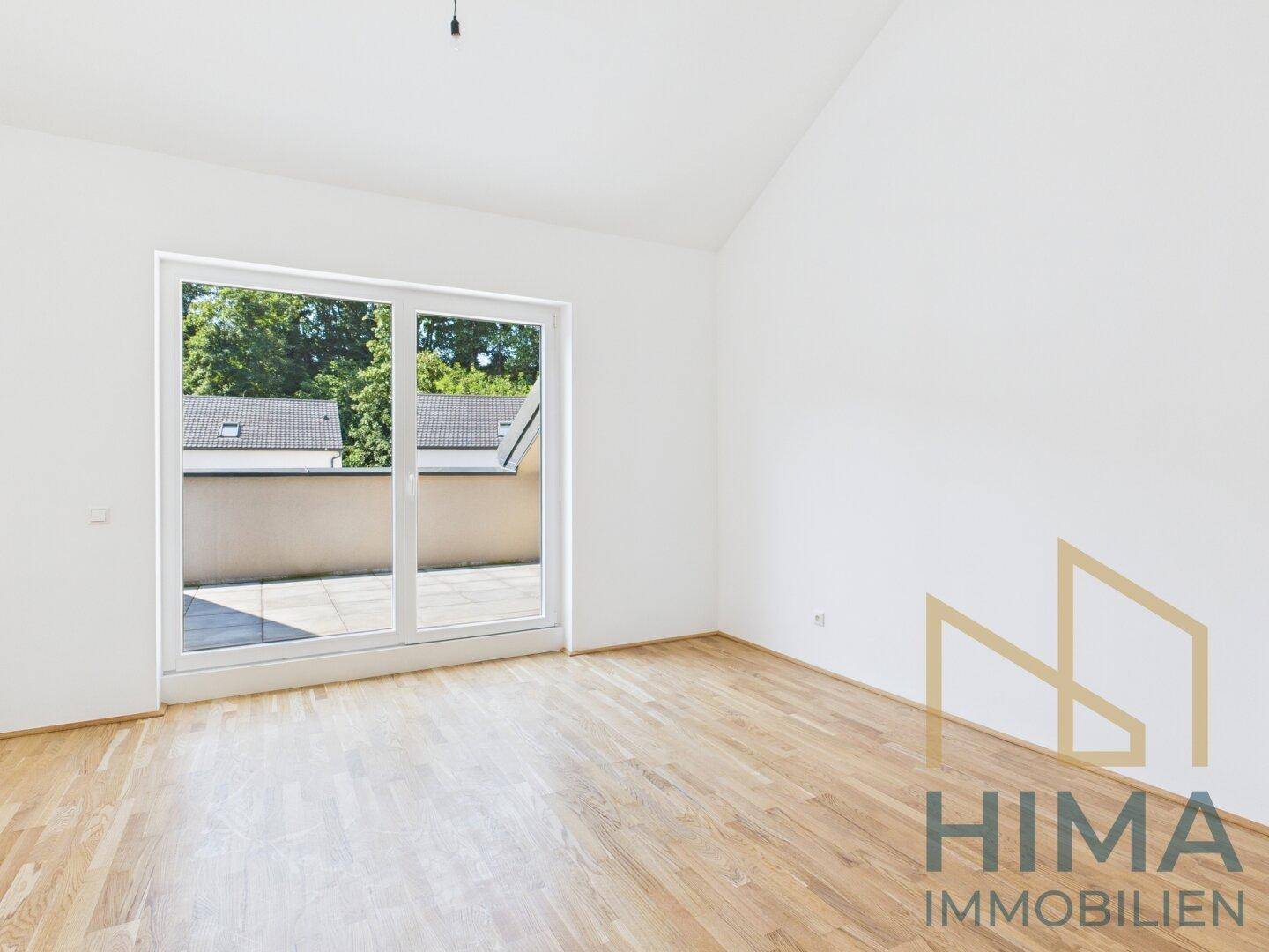 Helles Zimmer mit Parkettboden und großem Fenster, das Zugang zu einer Terrasse bietet.