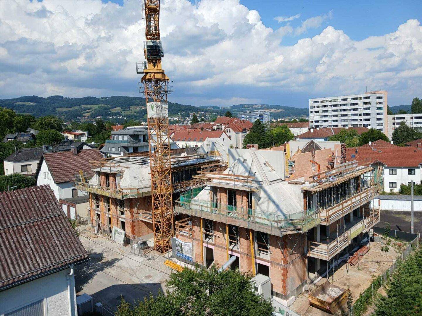 Zwei Neubauten im Rohbau mit Kran, umgeben von Wohngebäuden und städtischer Landschaft.