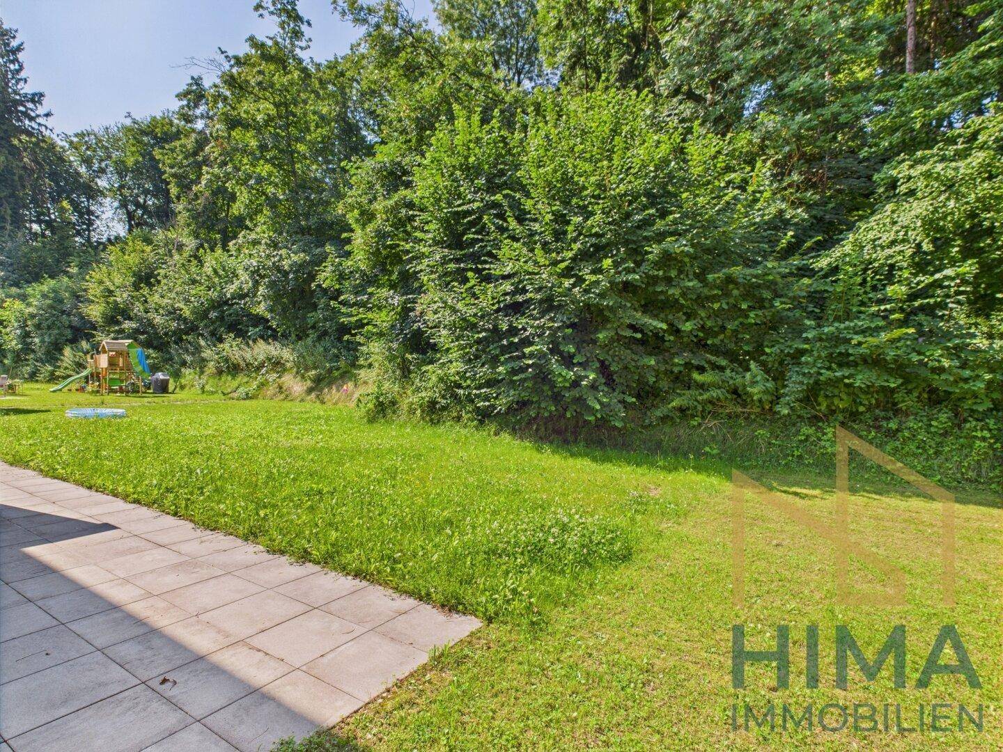 Großer Rasenbereich mit angrenzendem Wald und Spielplatz im Hintergrund.