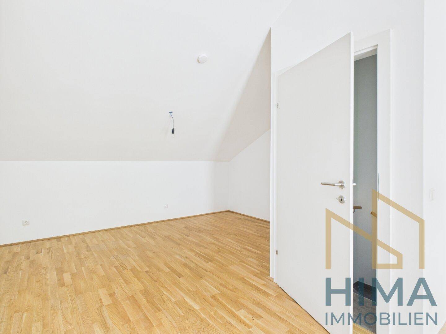 Dachgeschosszimmer mit Schrägen, hellem Parkettboden und weiß gestrichenen Wänden.