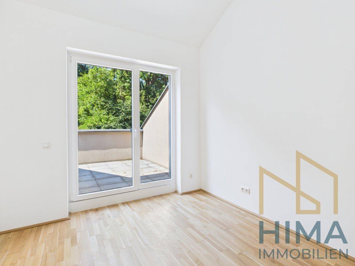Helles Zimmer mit Parkettboden und Zugang zu einem Balkon oder einer Terrasse.