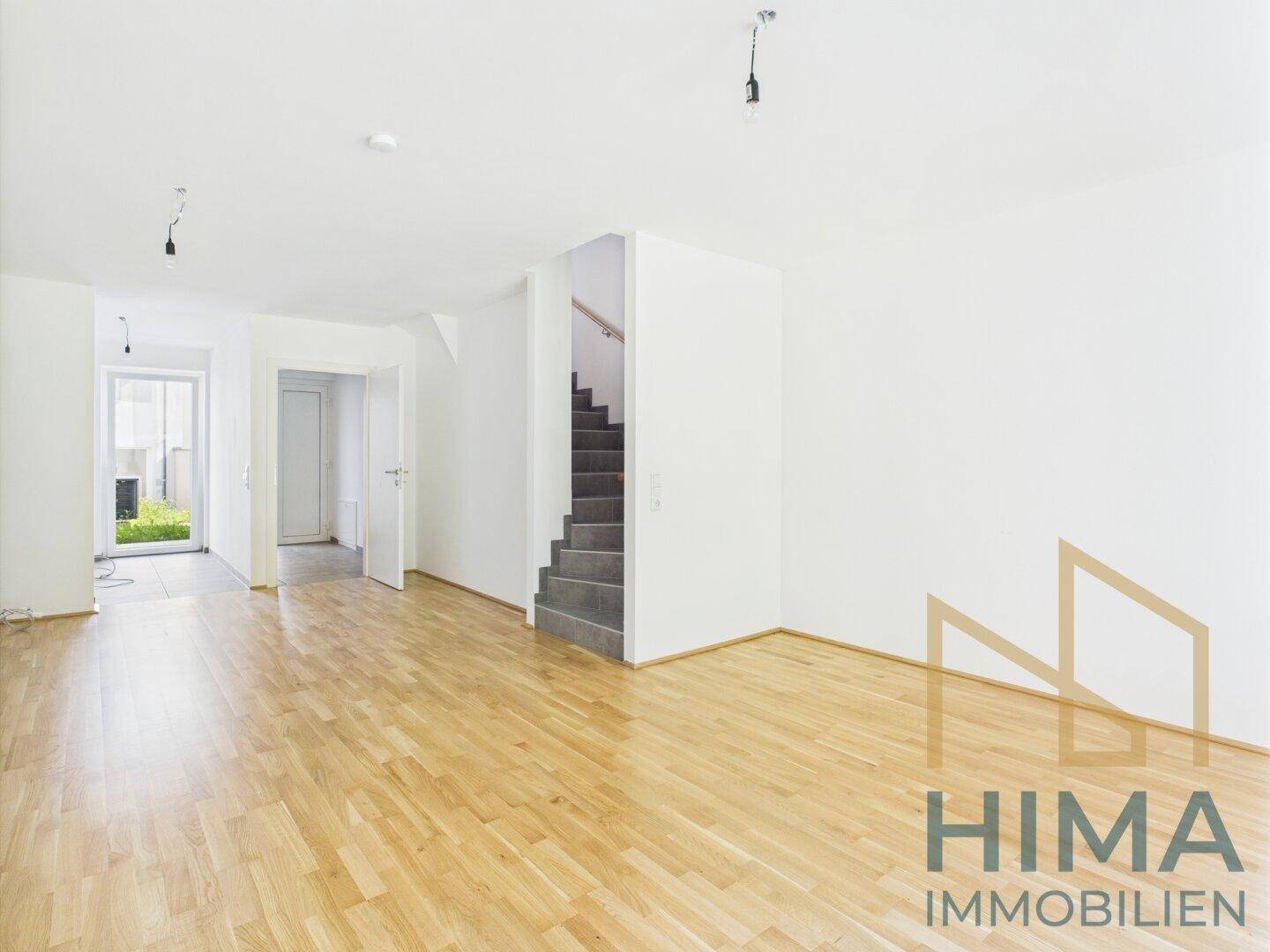 Geräumiges Wohnzimmer mit hellem Parkettboden und Treppenzugang.