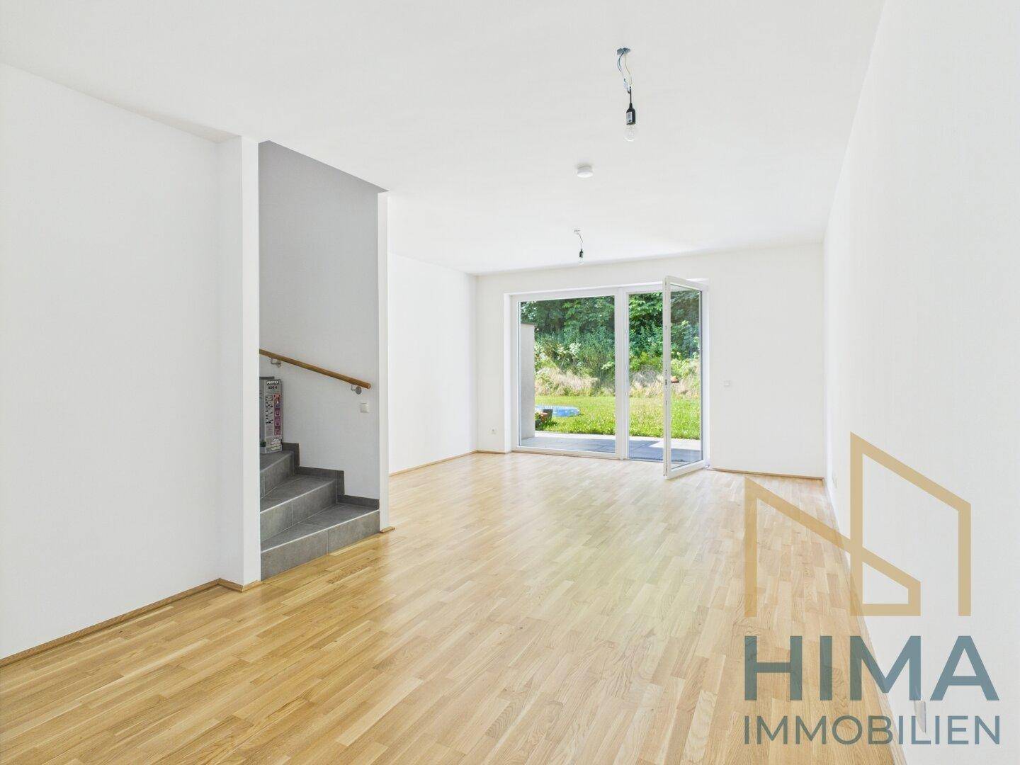 Helles, leeres Wohnzimmer mit Parkettboden und Zugang zum Garten.