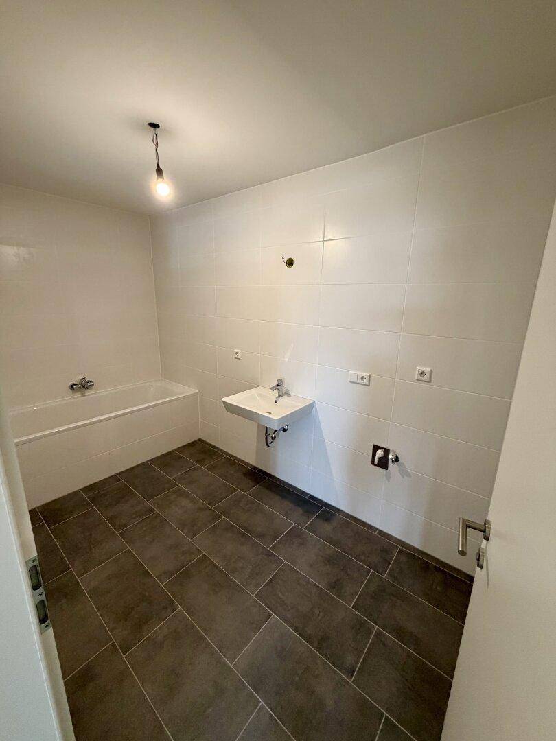 Modernes Badezimmer mit Badewanne, Waschbecken und dunklen Bodenfliesen, bereit zur Nutzung.
