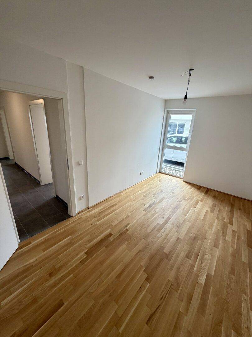 Leeres Zimmer mit Parkettboden und einem hohen Fenster, das viel Tageslicht in den Raum bringt.