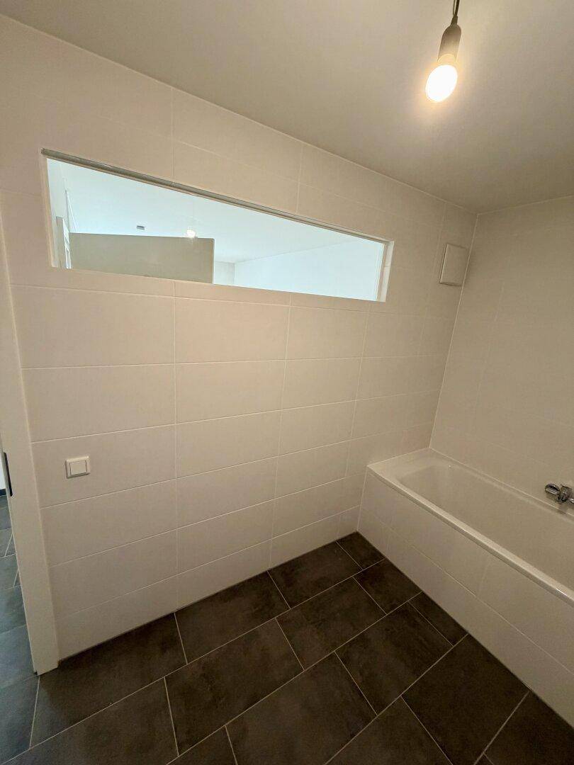 Badezimmer mit Badewanne und weiß gefliesten Wänden, ergänzt durch ein schmales Oberlichtfenster.