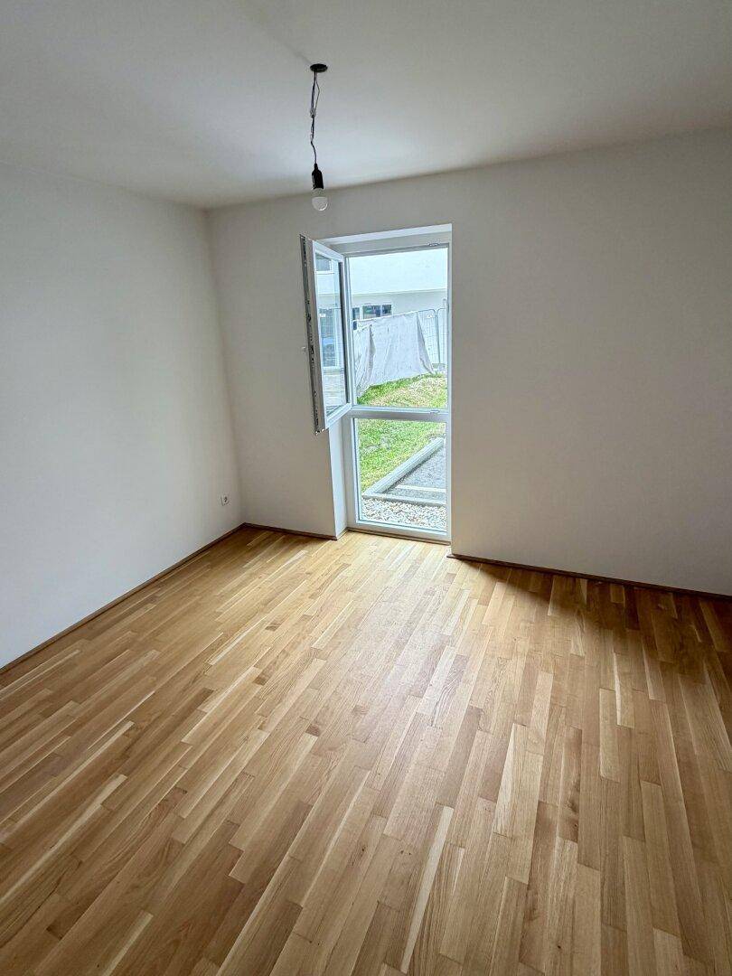 Leeres Zimmer mit Parkettboden und einem geöffneten Fenster, das frische Luft und Licht hereinlässt.