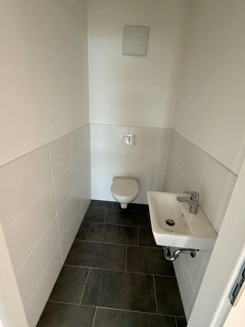 Kleines Gäste-WC mit wandhängender Toilette, Waschbecken und modernen Fliesen am Boden.