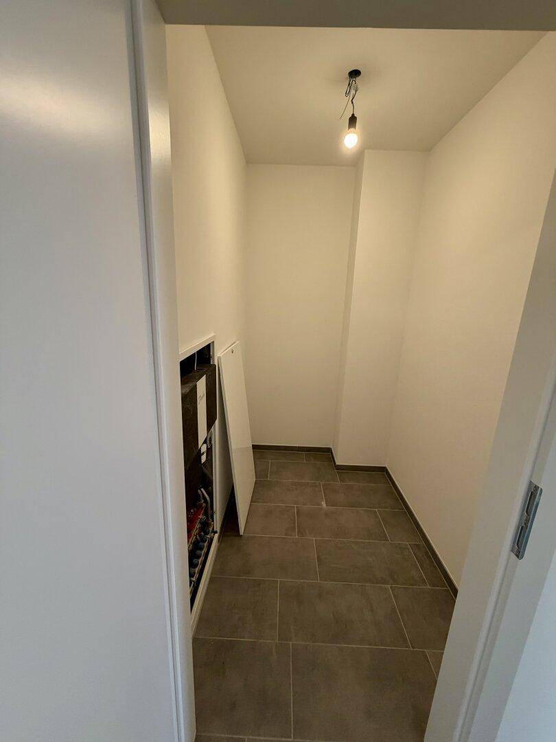 Praktischer Abstellraum mit Fliesenboden und sichtbaren technischen Installationen, ideal für Haushaltsgeräte.
