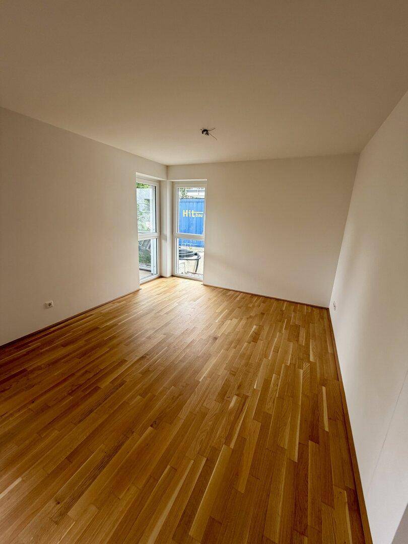 Leeres Schlafzimmer mit hellem Parkettboden und großen Fenstern, die viel Tageslicht hereinlassen.