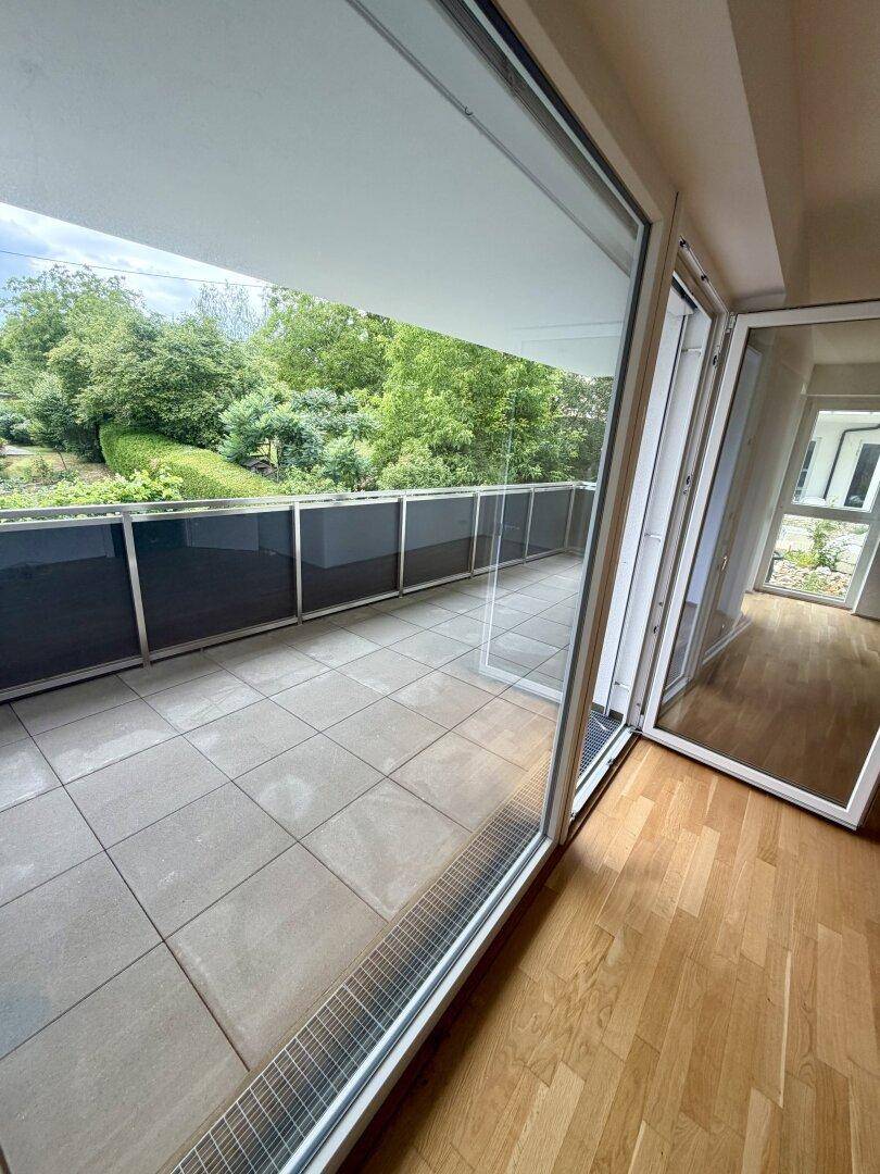 Geräumiger Balkon mit Fliesenboden und Blick ins Grüne, zugänglich durch große Glasschiebetüren.