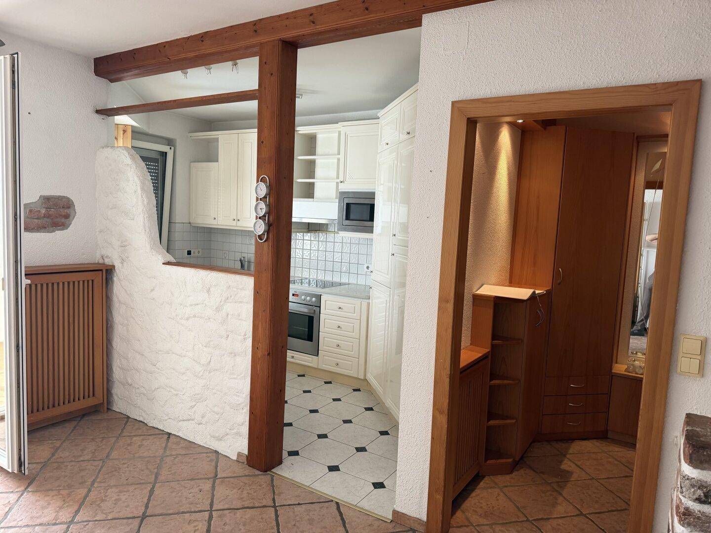Offener Wohn-Essbereich mit Holzbalken und Blick in die Küche mit Fliesenboden.