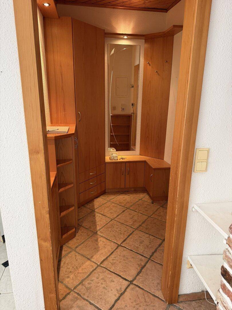 Eingangsbereich mit maßgefertigten Holzschränken, Spiegel und Terrakottafliesen.