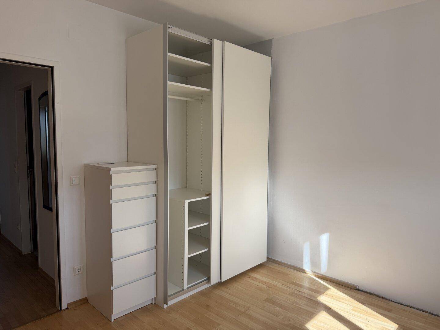 Schlafzimmer mit Laminatboden, weißen Wänden und einem modernen weißen Kleiderschrank.