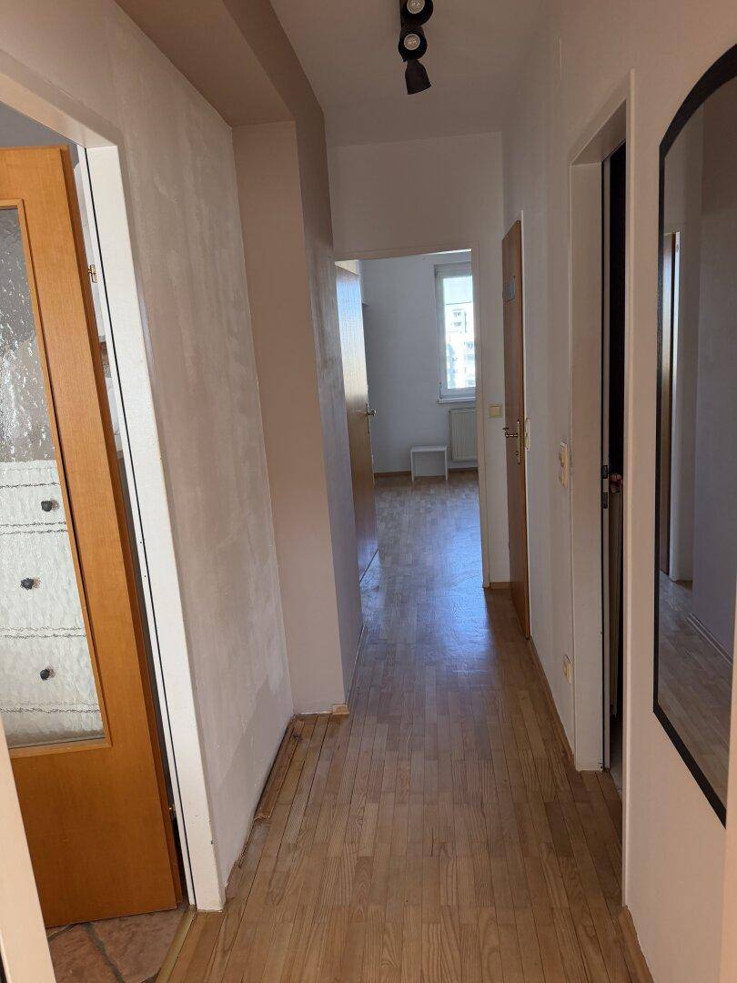 Langer Flur mit Laminatboden, der zu verschiedenen hellen Räumen der Wohnung führt.
