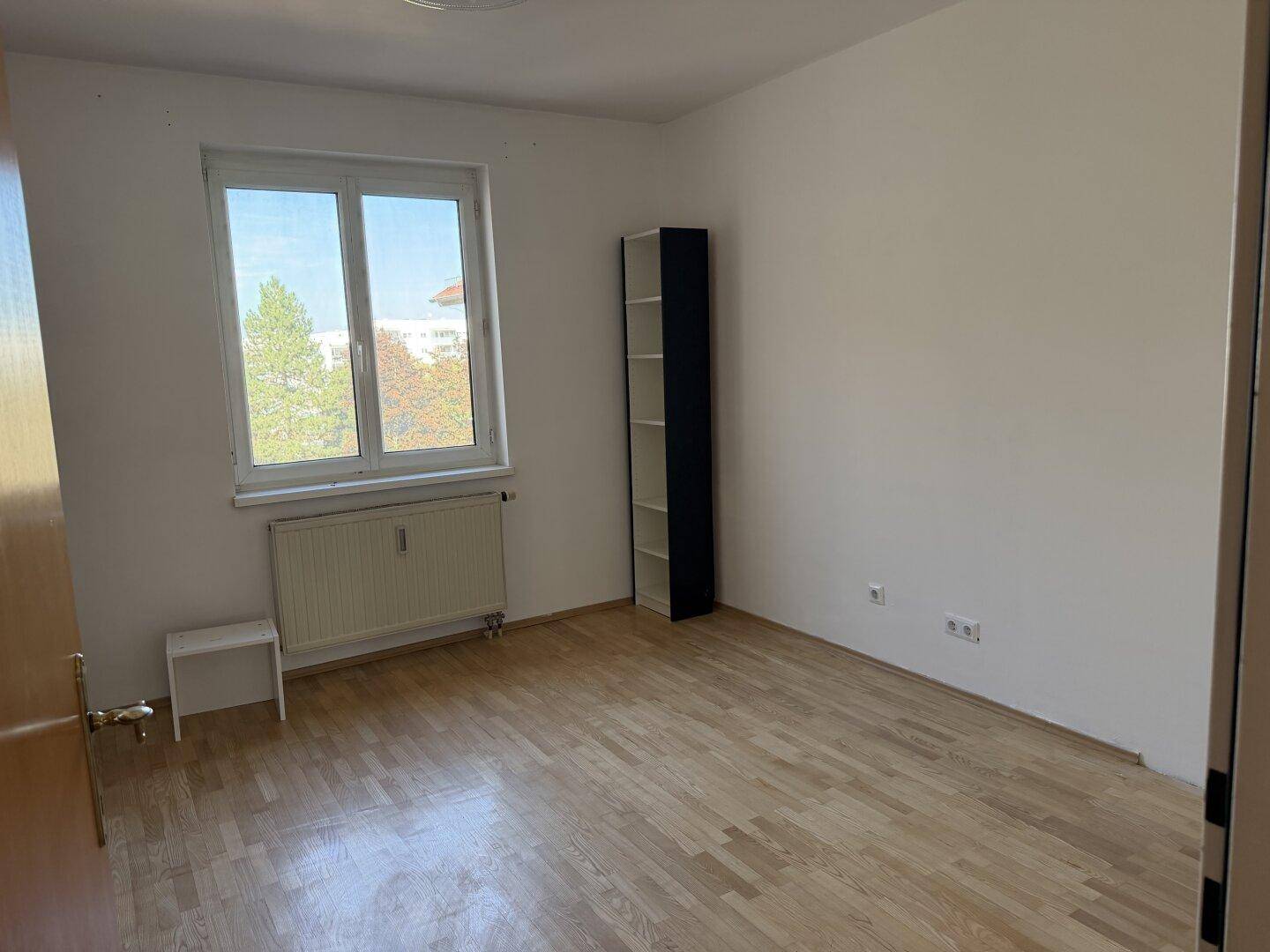 Geräumiges Schlafzimmer mit Laminatboden, weißen Wänden und Blick ins Grüne.