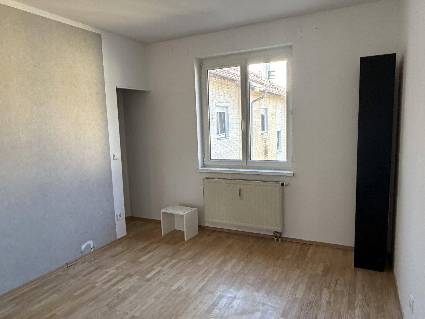 Helles Zimmer mit Laminatboden und Fenster, das einen Blick auf die Nachbarschaft bietet.