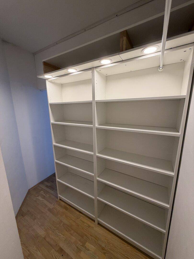 Begehbarer Kleiderschrank mit weißen Regalsystemen und integrierter Beleuchtung für optimale Organisation.