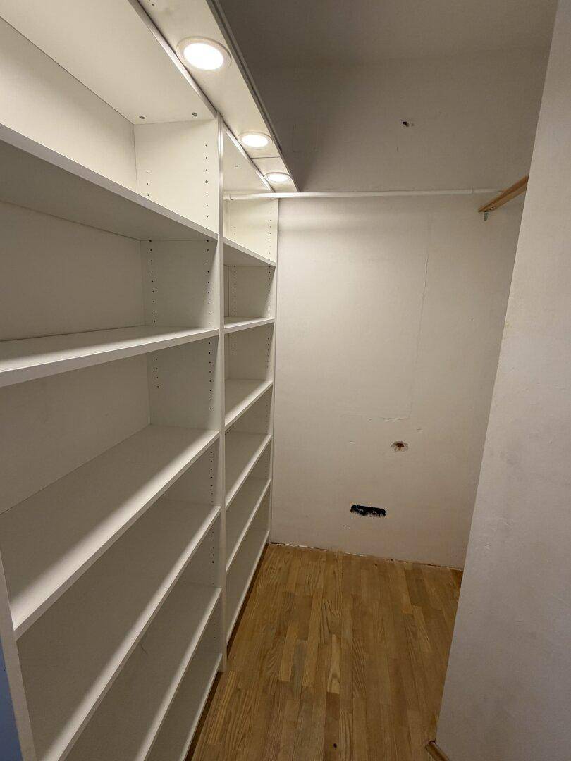 Praktischer begehbarer Kleiderschrank mit weißen Regalen und viel Stauraum.