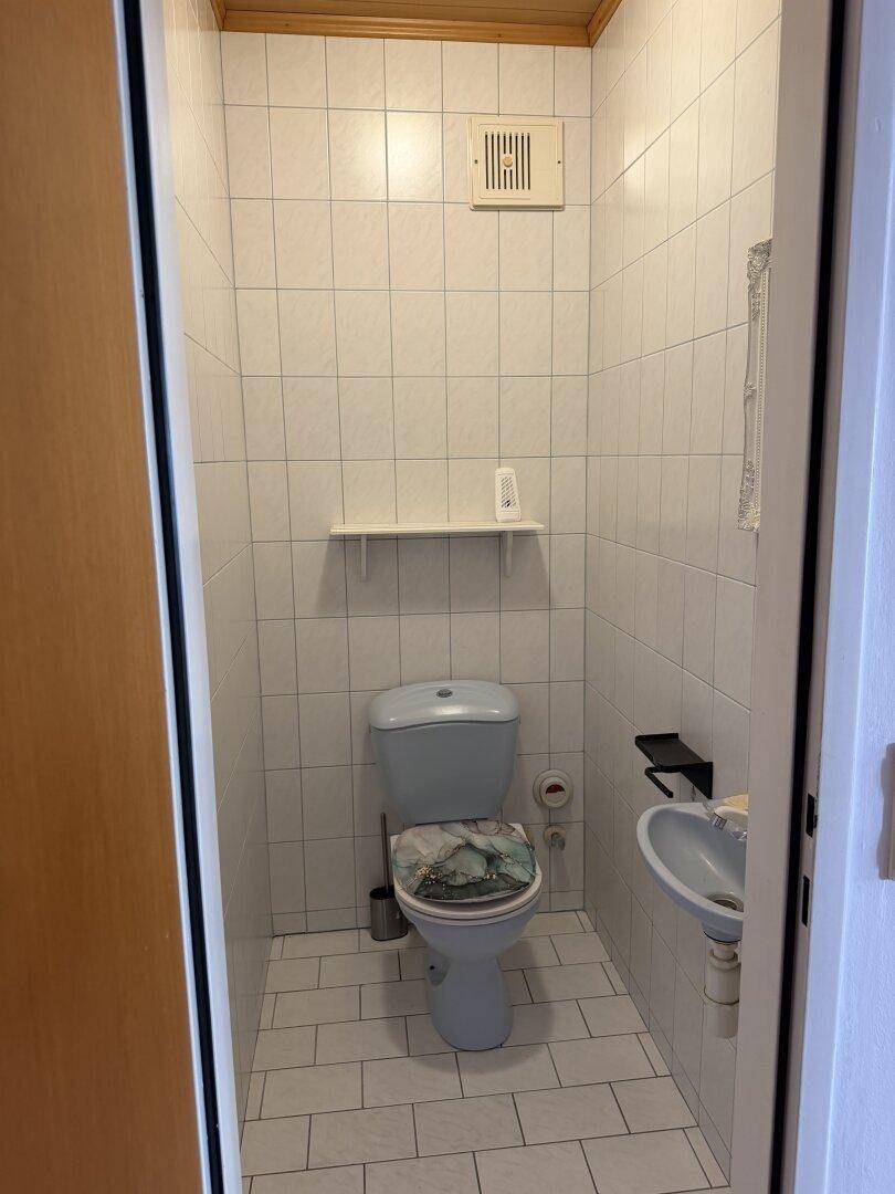 Kleines Gäste-WC mit hellblauer Toilette, Waschbecken und weißen Wandfliesen.