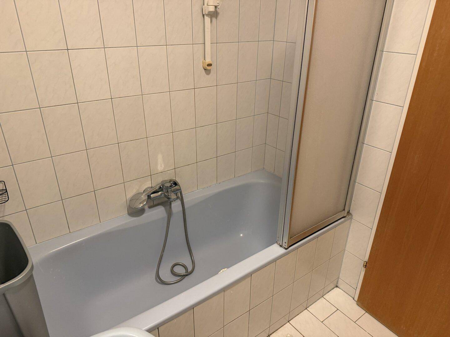 Badezimmer mit Badewanne, Duschabtrennung und weißen Fliesen, funktional und hell.
