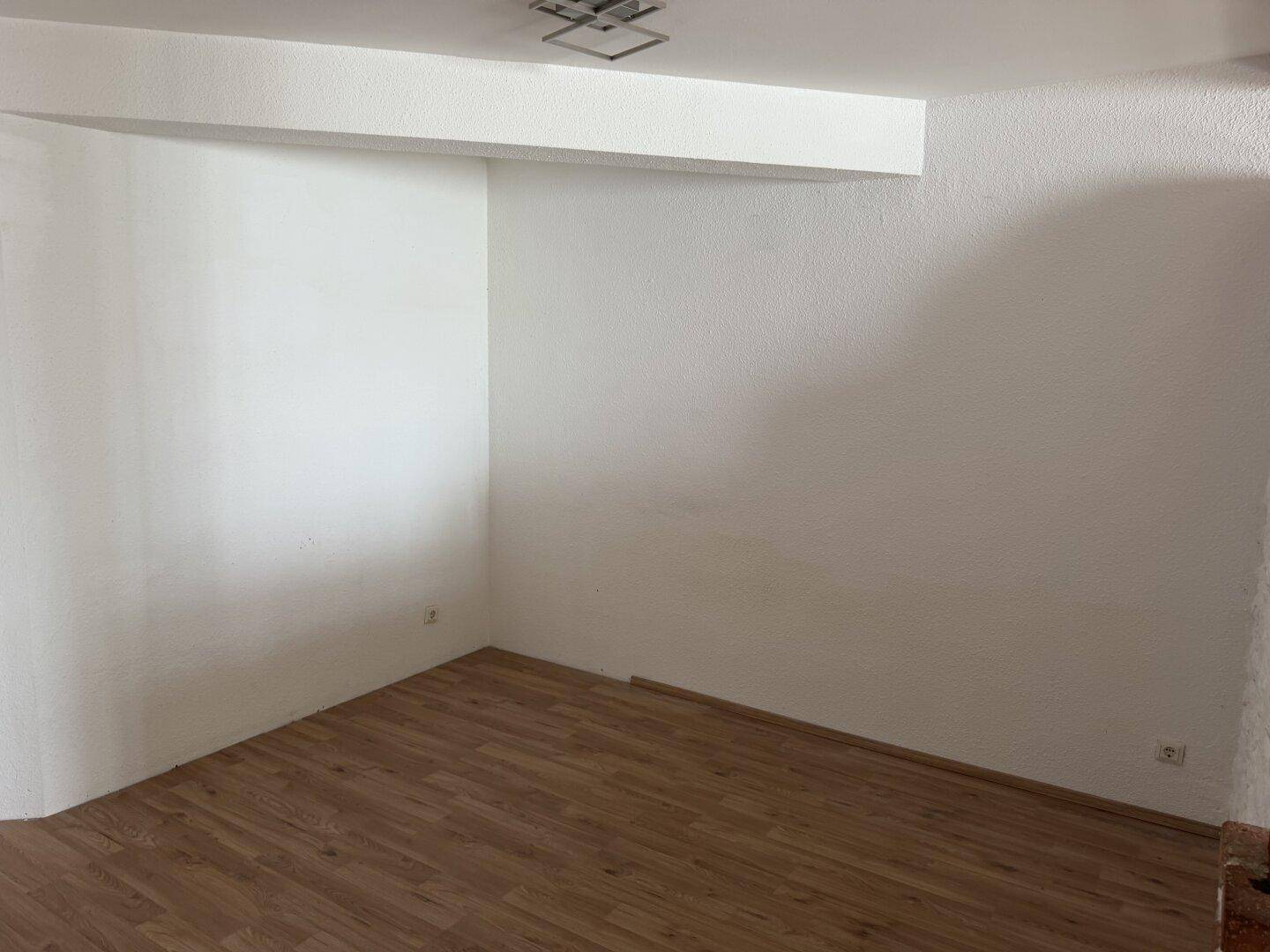 Leerer Raum mit hellem Laminatboden und weißen Wänden, bereit zur individuellen Gestaltung.