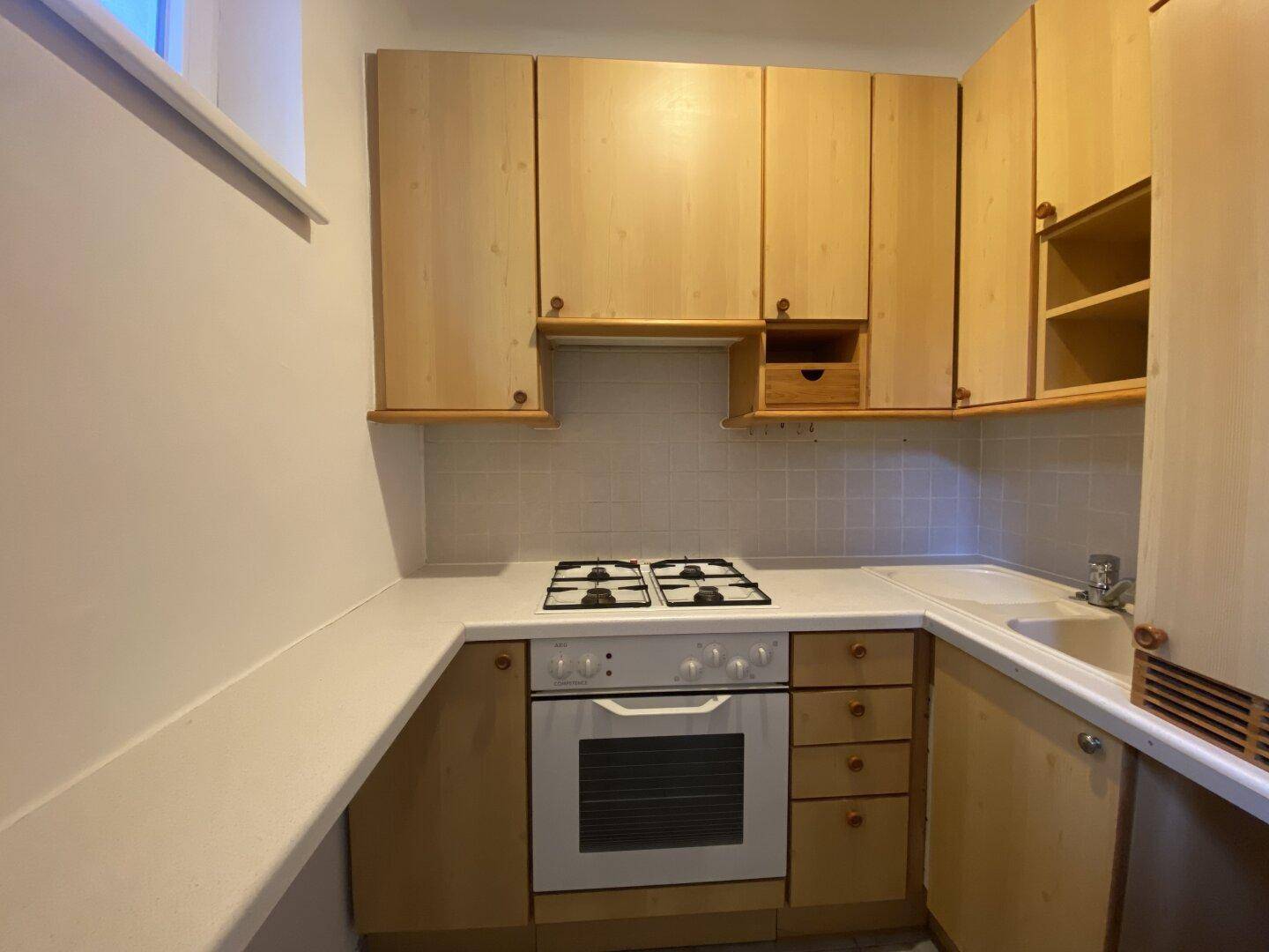 Funktionale Küche mit hellen Holzschränken, Gasherd, Backofen und Fliesenrückwand.