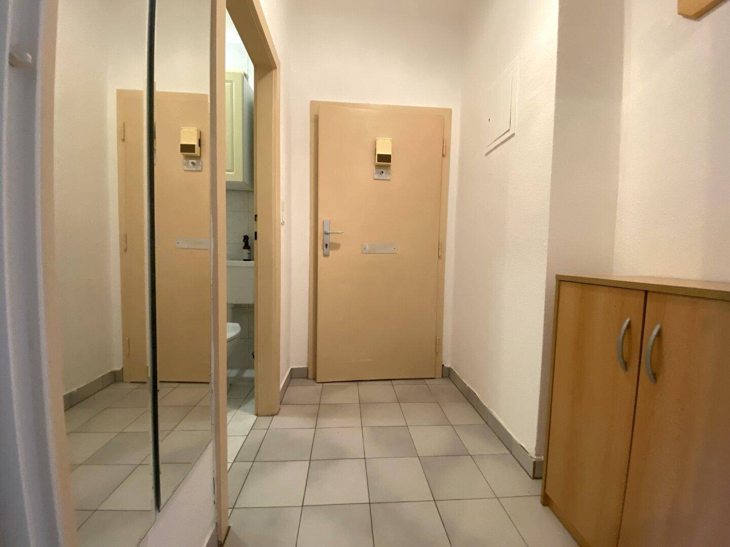 Heller Flur mit Fliesenboden, einem Holzschrank und Zugang zu weiteren Räumen.