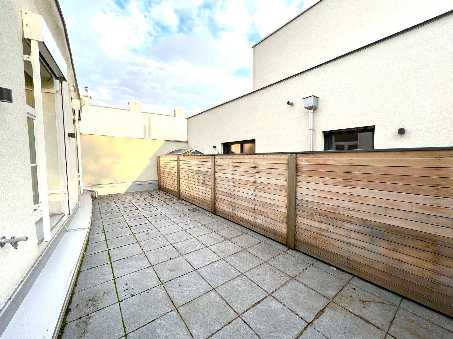 Weitläufige Terrasse mit moderner Holzverkleidung und Fliesenboden, umgeben von Gebäudefassaden.