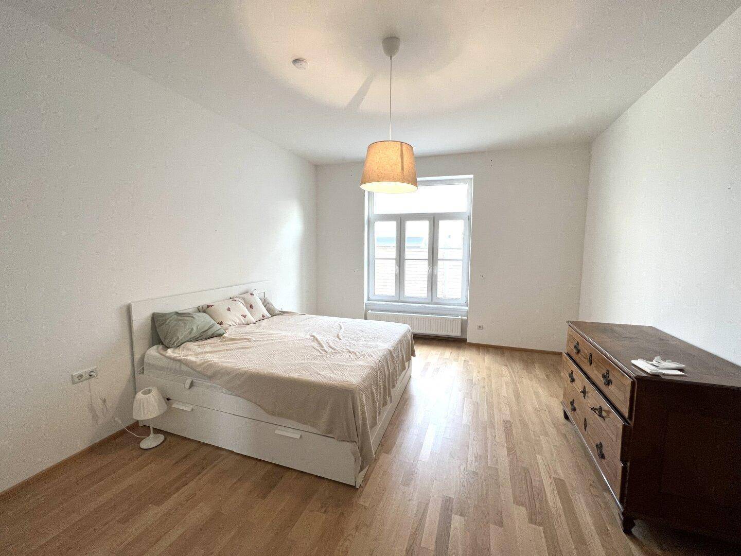 Gemütliches Schlafzimmer mit Doppelbett, Holzkommode und hellem Holzboden.
