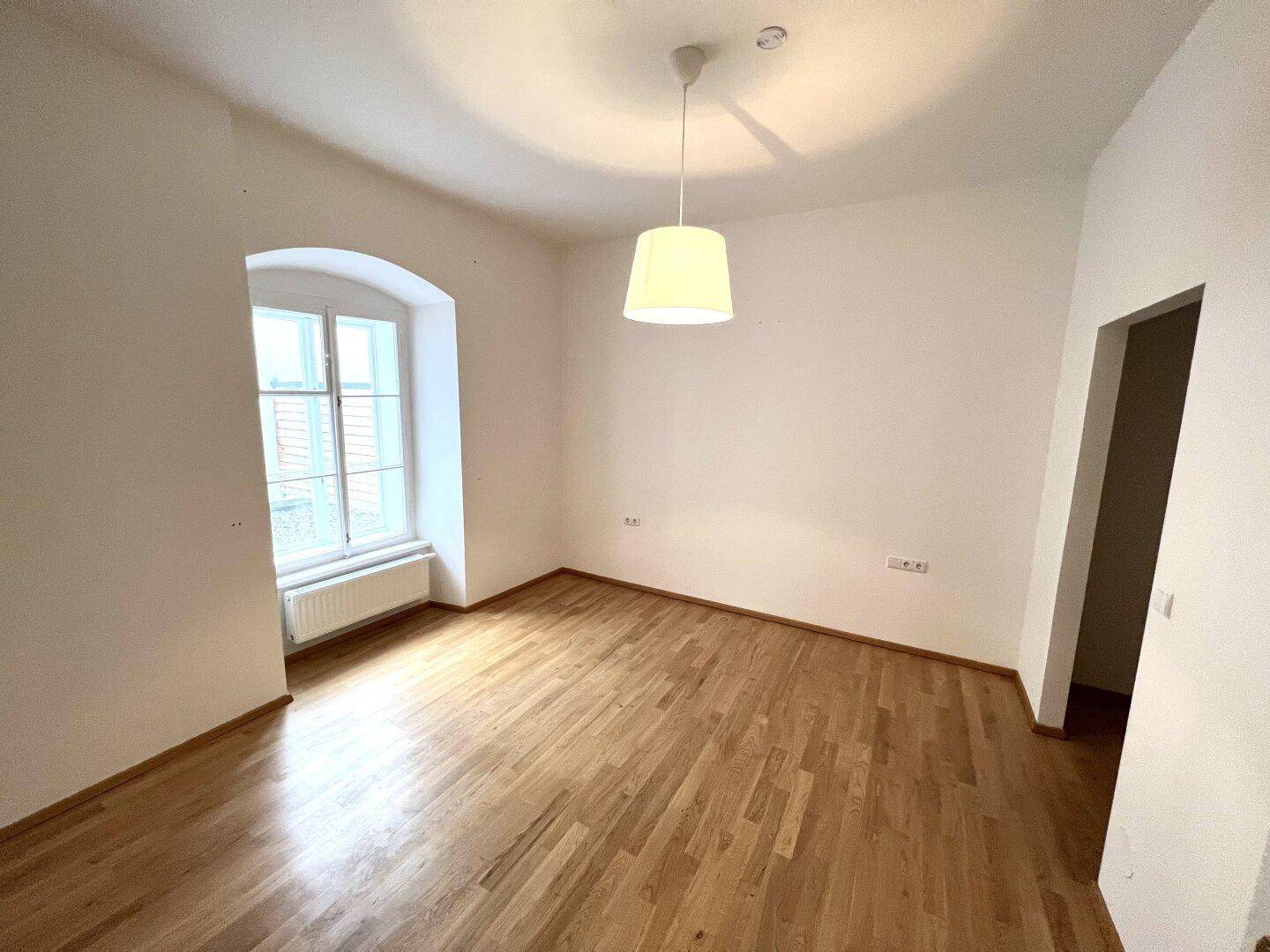 Leeres Zimmer mit Holzboden und einem charmanten Bogenfenster, bereit zur individuellen Gestaltung.