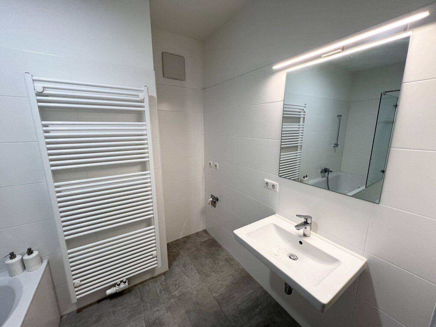 Modernes Badezimmer mit Waschtisch, beleuchtetem Spiegel und Handtuchheizkörper.