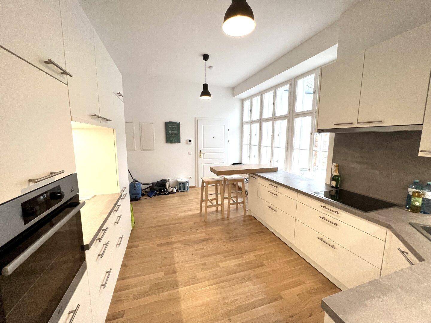 Offene Küche mit integrierten Geräten und Holzboden, Blick zum Eingangsbereich der Wohnung.