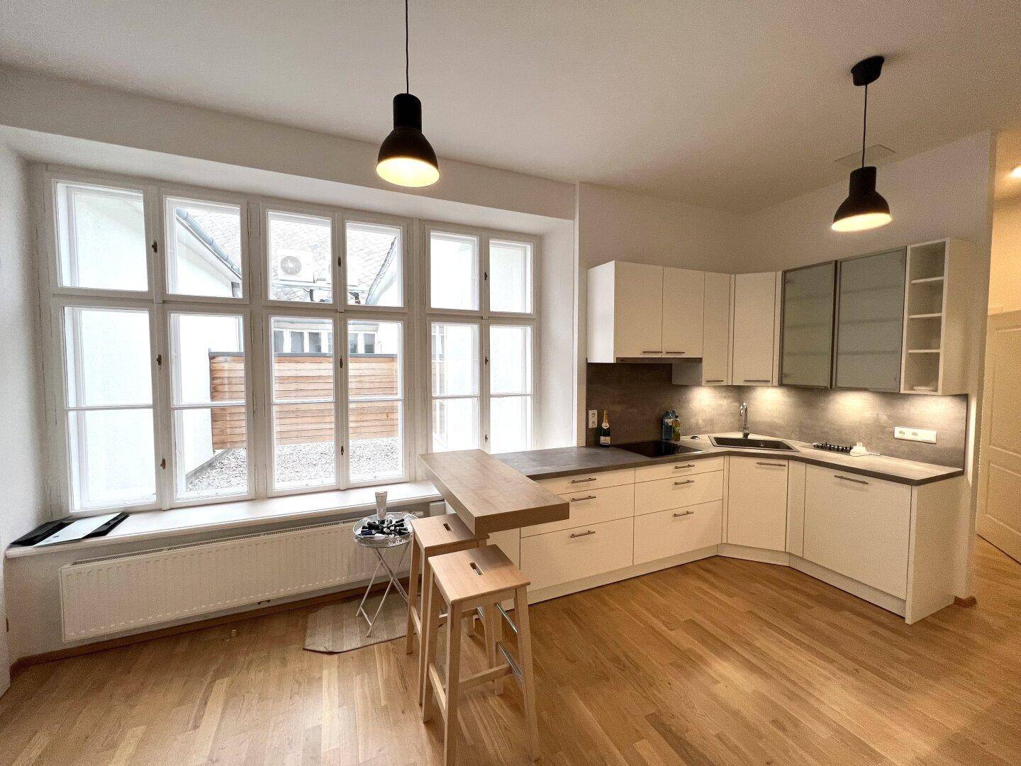 Helle, moderne Küche mit weißen Schränken, Holzarbeitsplatte und großem Fensterbereich.