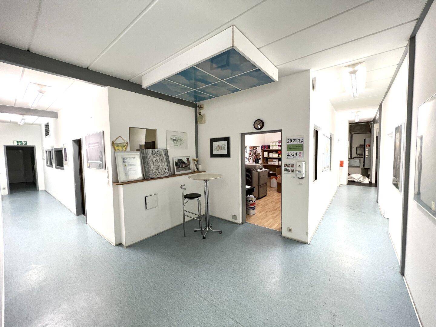 Empfangsbereich oder Gemeinschaftsraum mit Stehtisch, Bildern und Blick in angrenzende Büros.