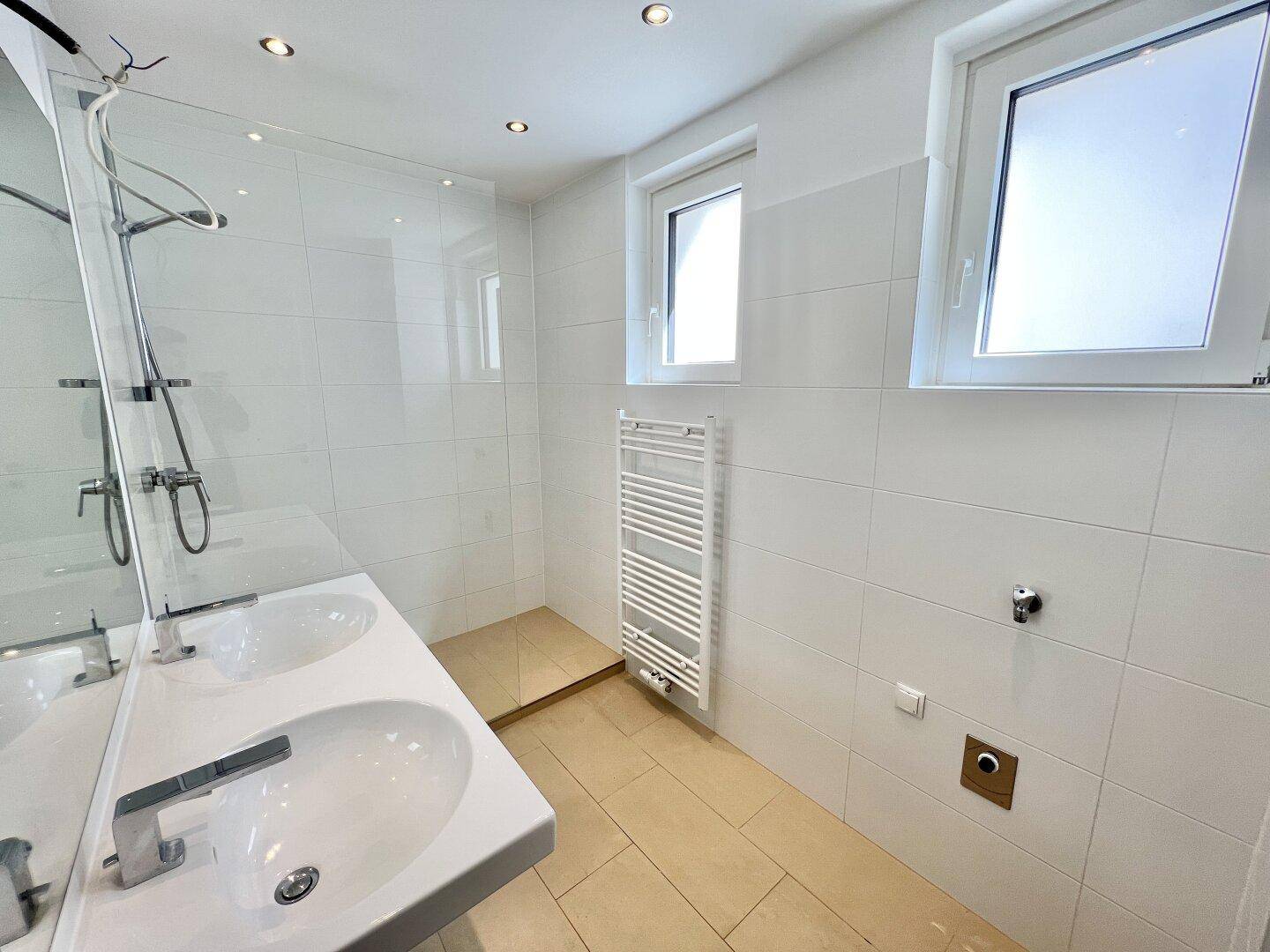 Modernes Badezimmer mit Doppelwaschbecken, ebenerdiger Dusche und zwei Fenstern.
