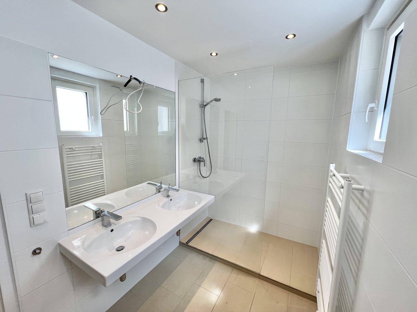 Geräumiges Badezimmer mit Doppelwaschbecken, großer Spiegelfläche und begehbarer Dusche.