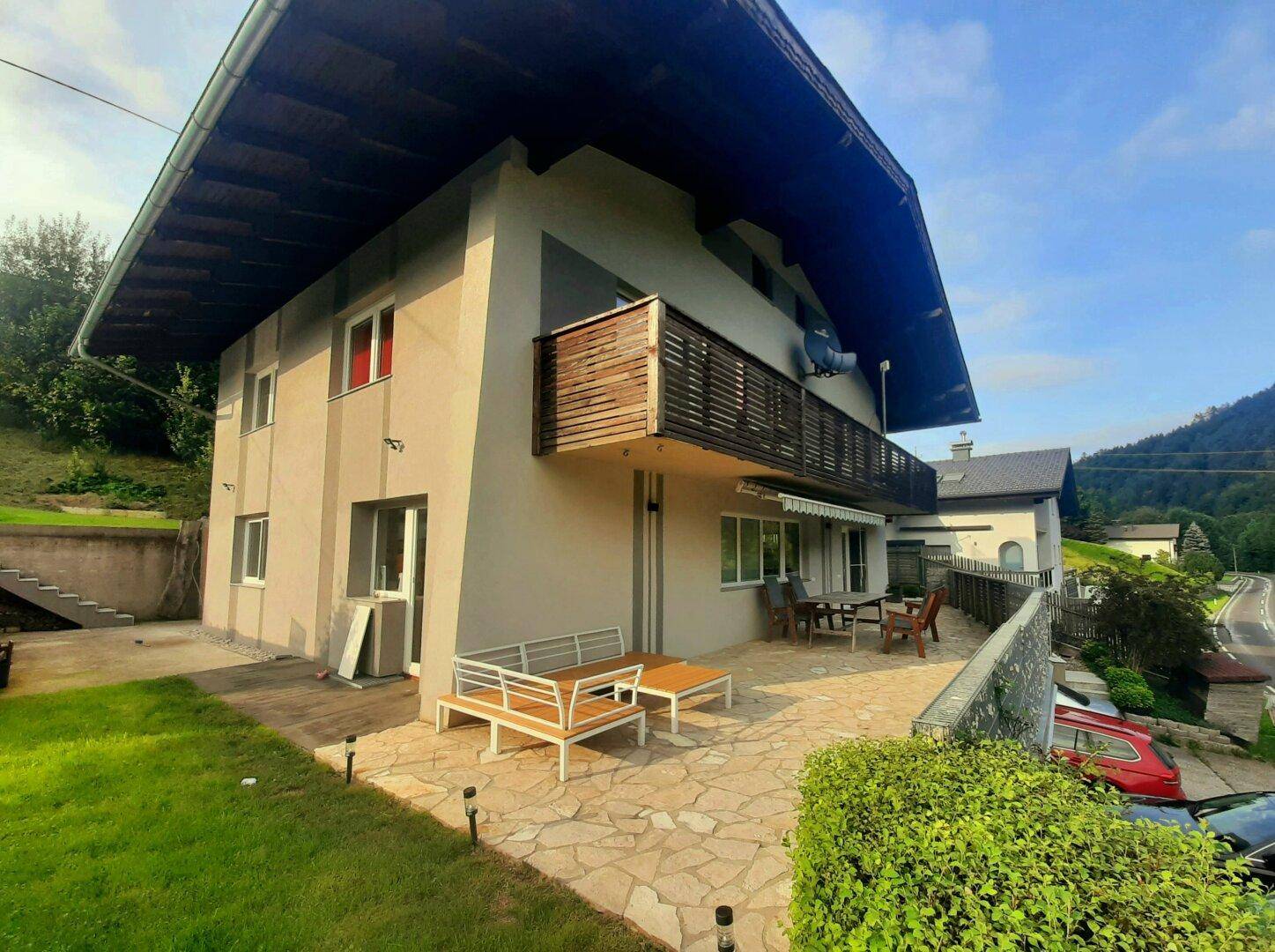 Modernes Haus mit großer gepflasterter Terrasse, Balkon und Sitzgelegenheiten im Freien.