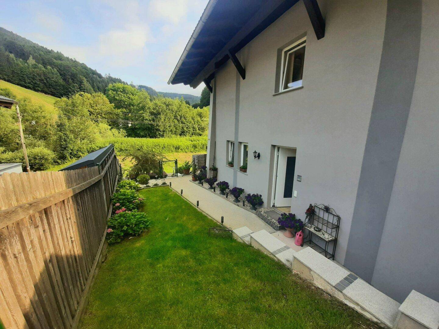Seitenansicht des Hauses mit Eingangsbereich, gepflegtem Rasen und grüner Umgebung.